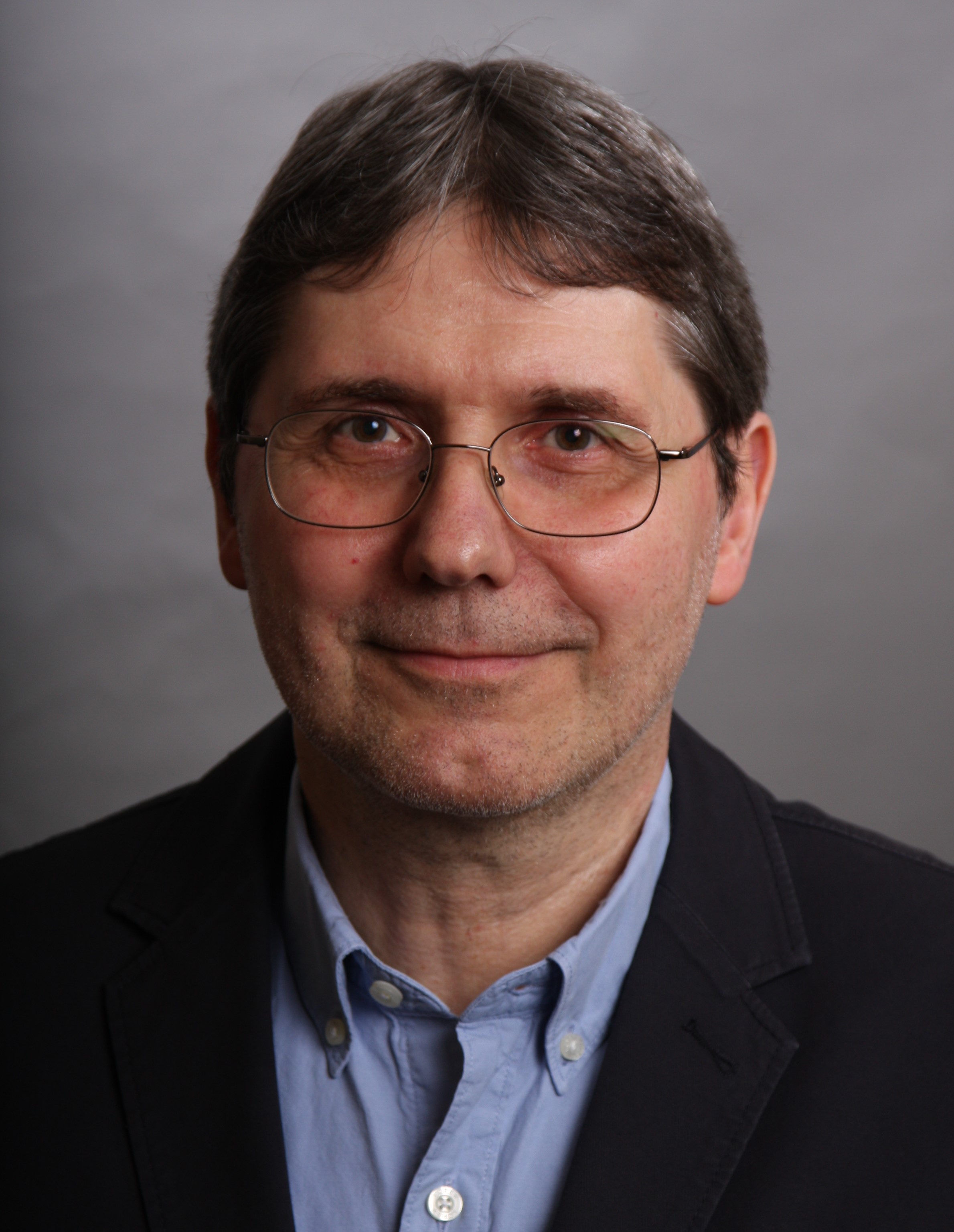 Headshot of male with glasses poses in front of grey background