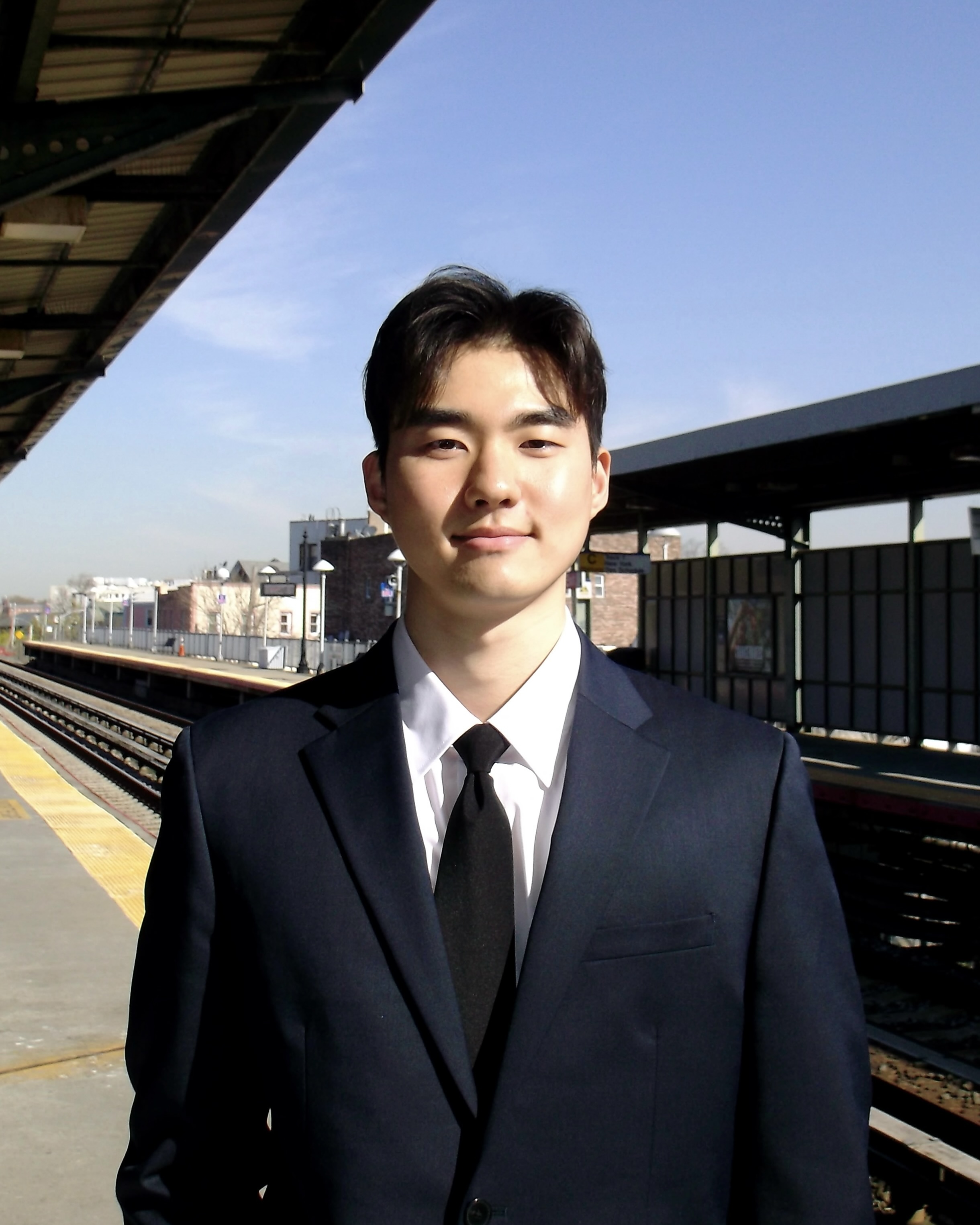Person in a business suit smiling at a train station platform on a sunny day.