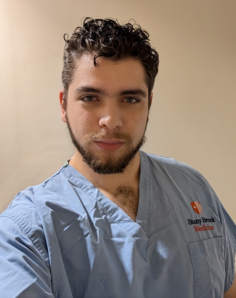 Person wearing a Stony Brook Medicine scrubs, standing in front of a beige background.