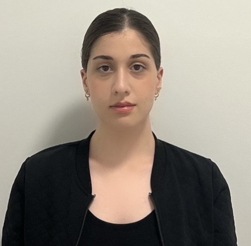 Portrait of a person with short hair, wearing a black top and small earrings, against a plain white background.