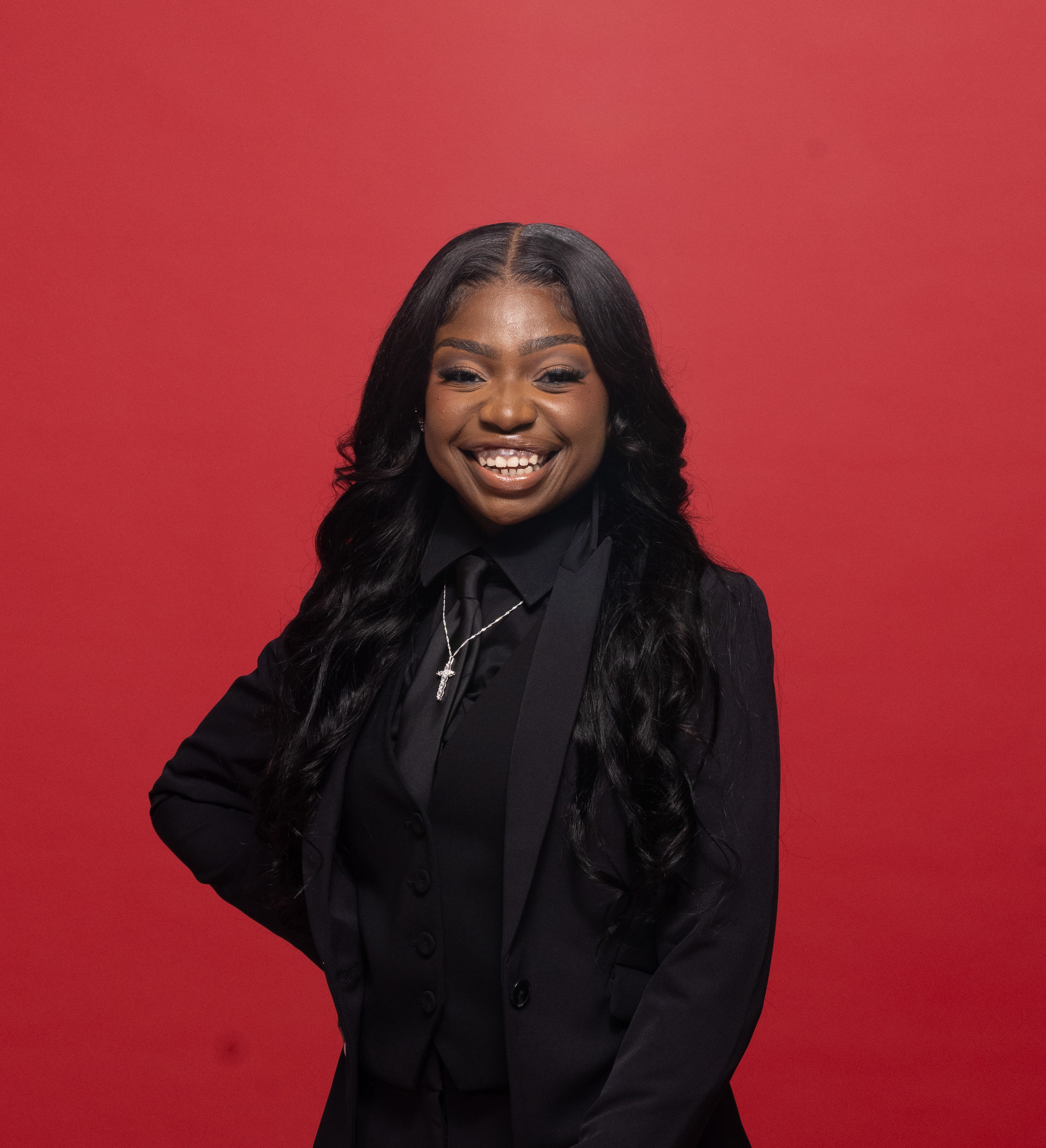 a woman smiles, hand on hip, standing in front of a red backdrop
