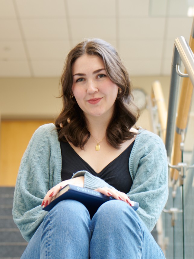 a smiling woman sits on a staircase with books on her lap