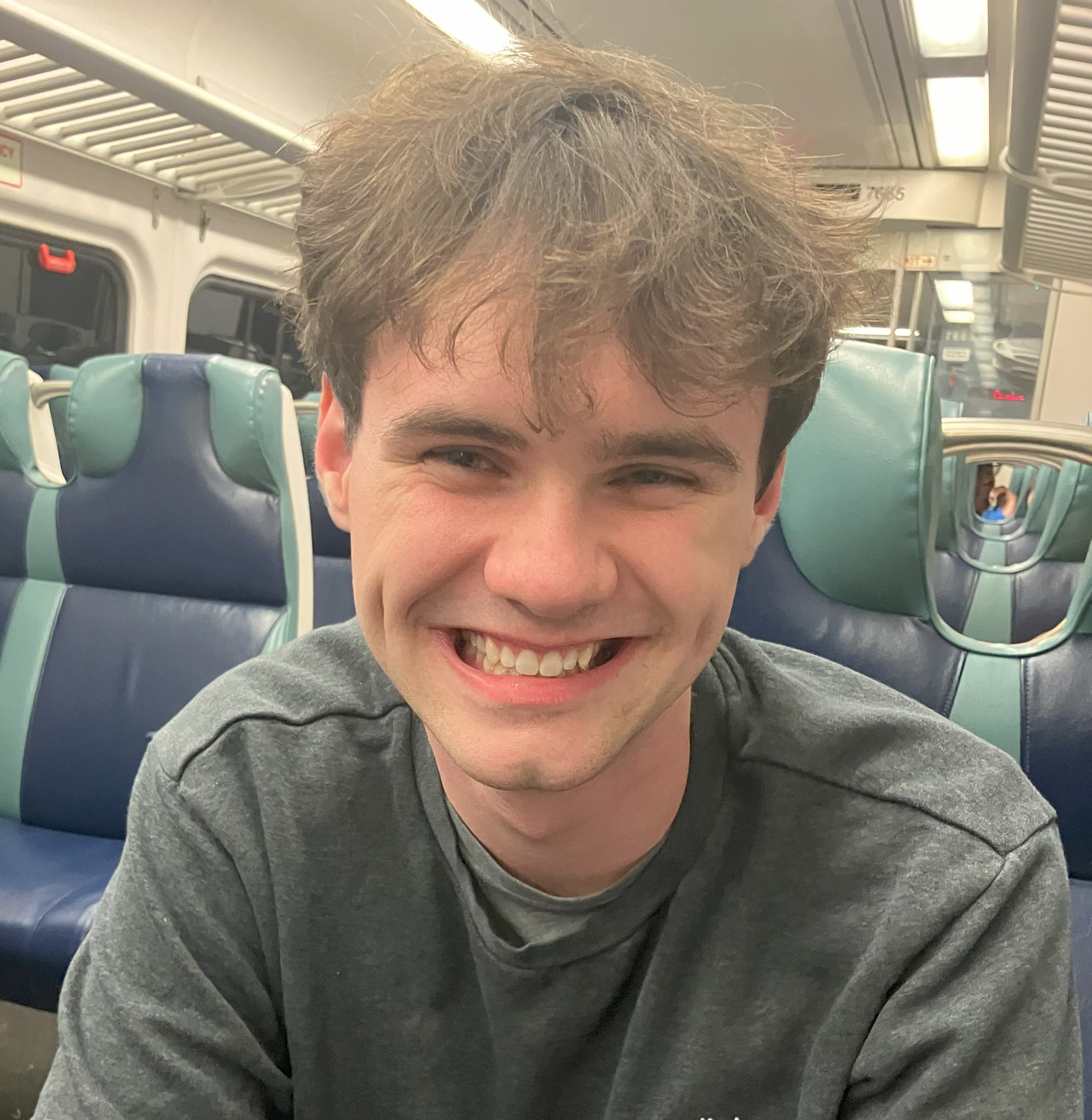 a smiling man sits in a seat on a commuter train 