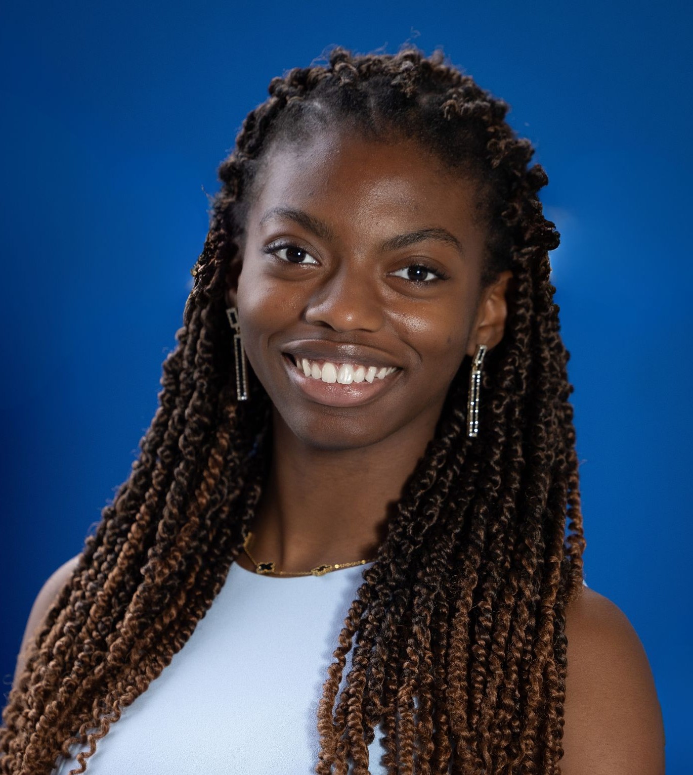 a smiling woman with braided hair poses in front of a blue backdrop