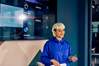 Woman standing in front of a large wall of monitors with visual representations of data