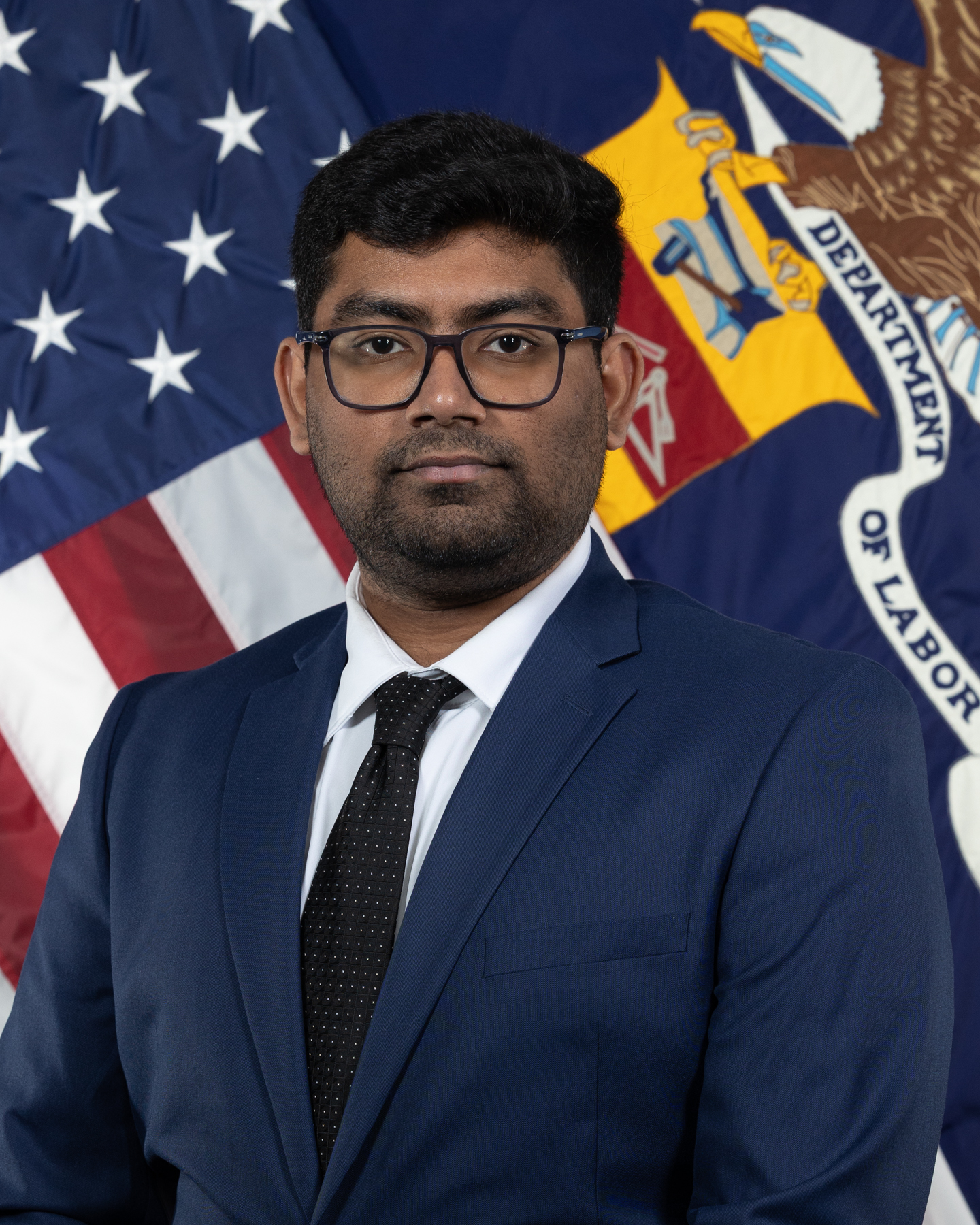 Dev posting in front of a flag of the United States and the Department of Labor.
