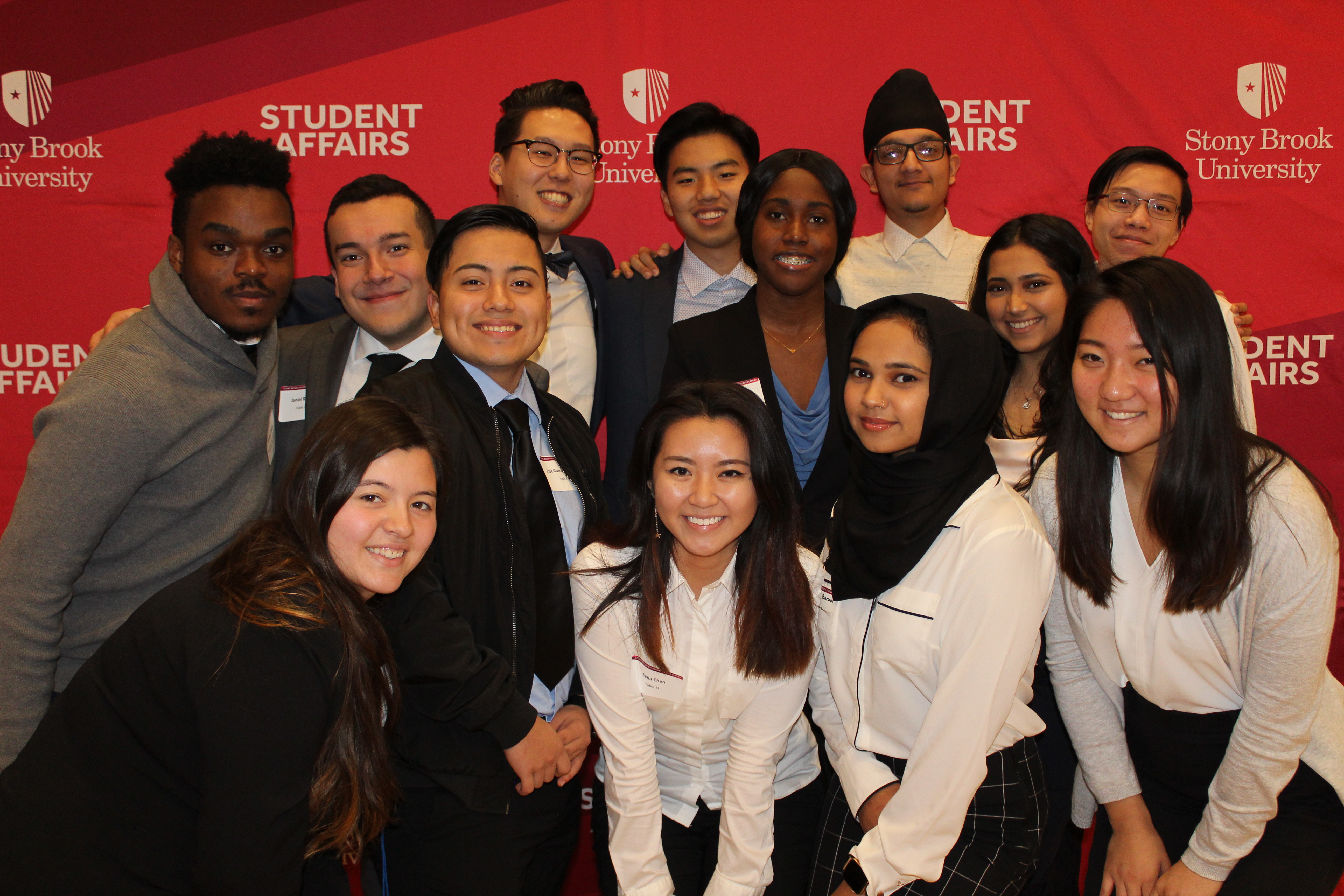 A group of graduate students gathered in front of a Student Affairs photo op backdrop