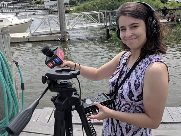 brunette student smiles at the camera, holding a WSHU microphone to conduct an interview