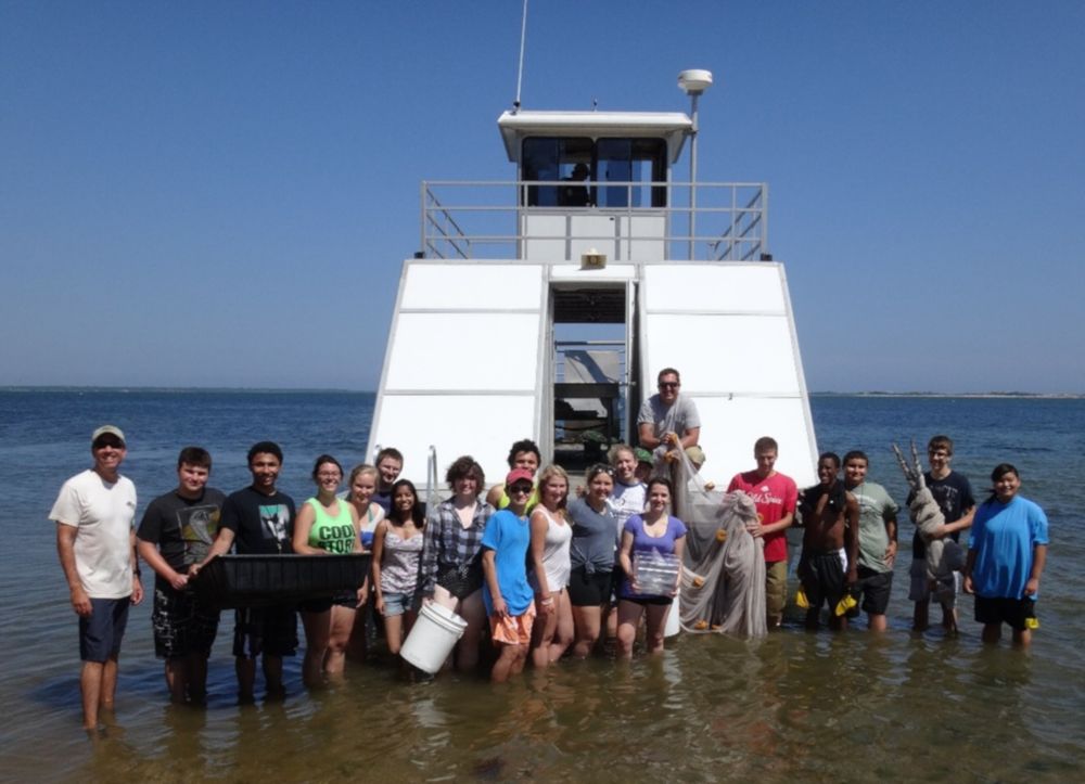 Students standing in water in front of a boat